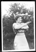 Vintage photo of a smiling woman folding her arms and pointing a handgun