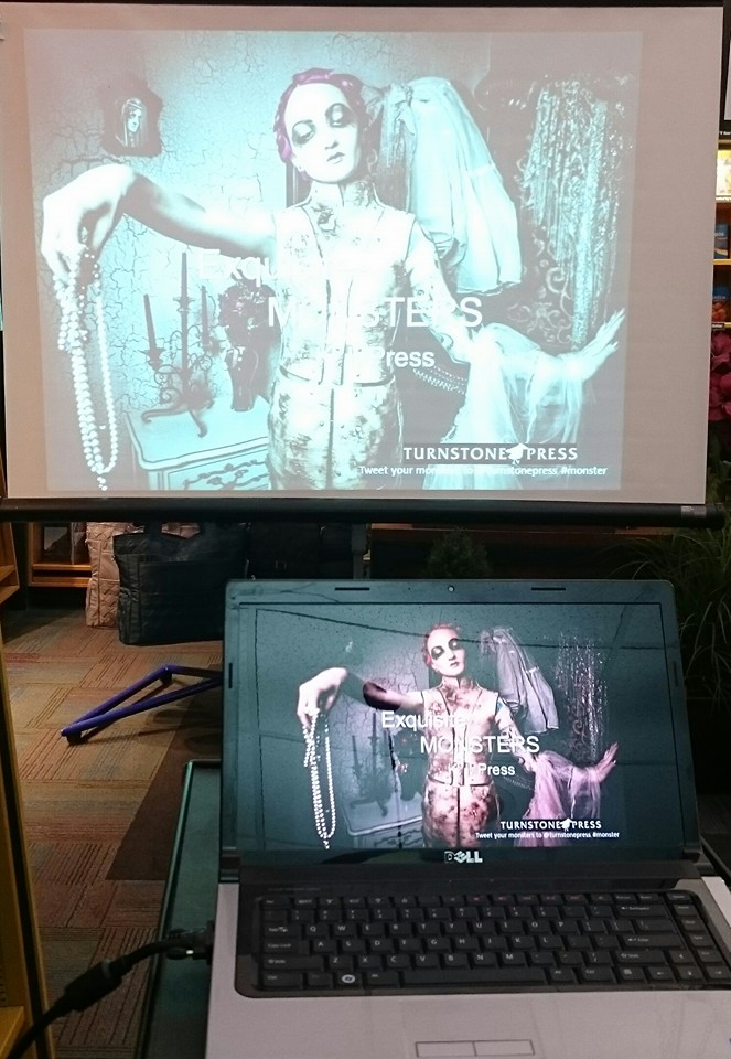 Image of a mannequin holding a pearl necklace, repeated on a laptop screen and projected on  screen in front of the laptop.